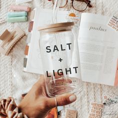 a person holding a glass jar with salt and light written on it next to other items