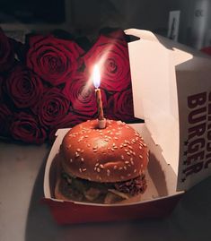 a hamburger with a lit candle in it sitting on top of a table next to a box