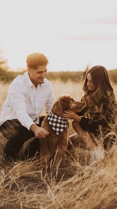 a man and woman sitting in the grass with their dog