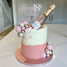 a birthday cake decorated with pink, white and gold decorations has a bottle of champagne on top