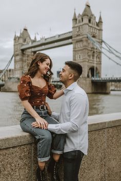 a man and woman sitting on the edge of a bridge