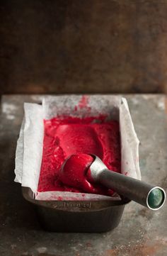 a bowl filled with red liquid sitting on top of a metal table next to a spoon