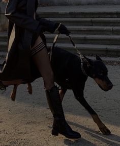 a woman is walking with her dog in the street while wearing boots and a coat