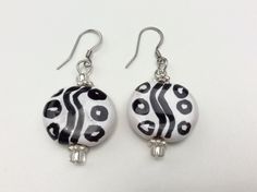 "These dynamic African earrings are made from glossy white Kazuri beads decorated with a bold black design.  They are handmade from African fair trade ceramic beads. The fish hook wires are hypoallergenic stainless steel.  These beautiful earrings are surprisingly lightweight weighing 0.2 oz. The earrings are about 2 inches // 55 mm long. The beads are approximately 3/4 inch // 22-23 mm.  Handmade Each bead is fashioned out of Mt. Kenyan clay, hand-shaped and fire-glazed in brick kilns.  When I Gift White Beaded Earrings With Black Beads, Nickel-free White Beaded Round Earrings, Nickel-free White Round Beaded Earrings, Black Earrings With Large Round Beads, White Nickel-free Round Beaded Earrings, White And Black Beaded Earrings, Kazuri Beads, Lady Susan, Clay Hand