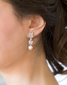 a close up of a woman's face wearing earrings with flowers on them and pearls hanging from the ear