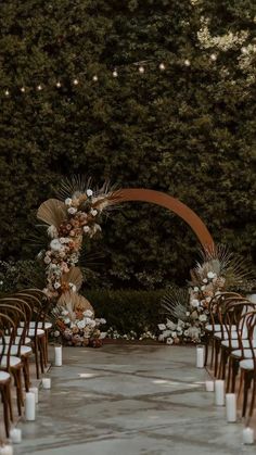 an outdoor ceremony setup with white candles and flowers on the aisle, surrounded by greenery