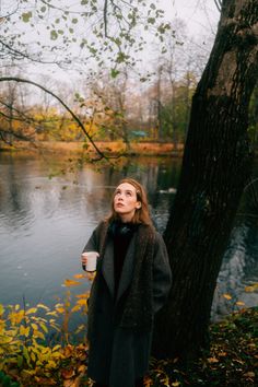 a woman standing next to a tree holding a coffee cup