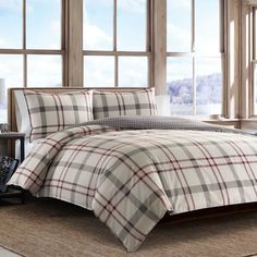 a bed with plaid comforter and pillows in front of a large window on the floor