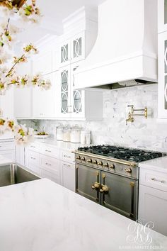 a white kitchen with marble counter tops and stainless steel stove top oven, sink, and cabinets