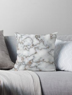 a white and gold marble pillow on a gray couch with two pillows next to it