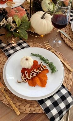 a white plate topped with an orange leaf next to a wine glass and pumpkins