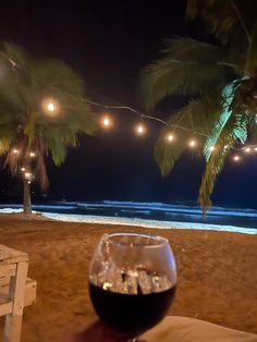 a glass of wine sitting on top of a sandy beach next to the ocean at night