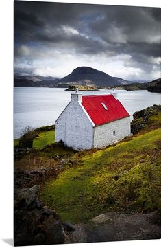 a white house with a red roof sitting on the side of a hill next to a body of water