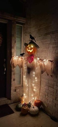 a lighted scarecrow standing in front of a brick wall with pumpkins on the ground