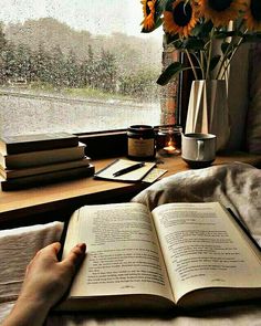 an open book sitting on top of a bed next to a vase with sunflowers