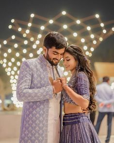 a man and woman standing next to each other in front of some string lights at night