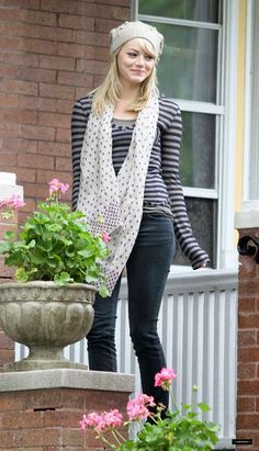 a woman standing next to a potted plant on a porch with flowers in it