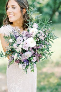 a woman holding a bouquet of flowers and greenery in front of her face, smiling at the camera