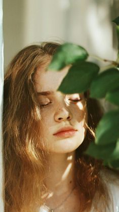 a woman with her eyes closed standing next to a plant