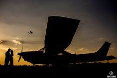 the silhouette of two people standing next to an airplane at sunset with a plane in the background