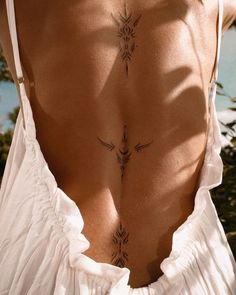 the back of a woman's white dress with tattoos on her upper and lower back