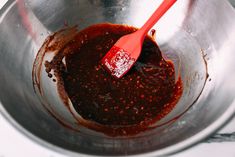 a metal bowl filled with sauce and a red spoon