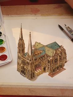 a drawing of a cathedral with paint and watercolors on the table next to it