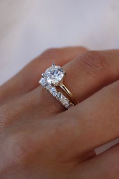 a woman's hand with a diamond ring on top of her finger and the other hand holding an engagement ring