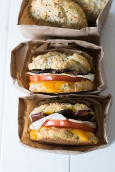 two sandwiches with cheese, tomatoes and sausage in paper wrappers on a white surface