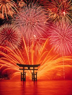 fireworks in the sky over water and a building with a bench on it's side