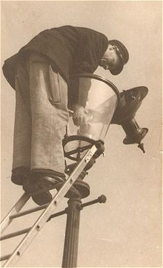 an old photo of a man working on a lamp post