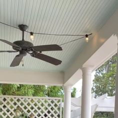 a ceiling fan on the outside of a house with white pillars and latticed fence