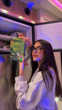 a woman holding up a box of broccoli in front of an open refrigerator