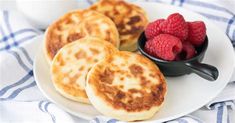 three pancakes with raspberries on a white plate next to a bowl of berries