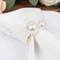 two white pearls are sitting on top of a napkin with flowers in the back ground