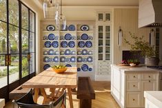 a wooden table sitting inside of a kitchen next to a wall filled with blue and white plates