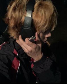 a man with blonde hair is holding a cell phone to his ear and looking at the camera