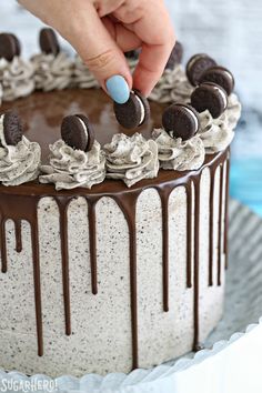 someone decorating a cake with chocolate and oreo cookies on top, ready to be eaten