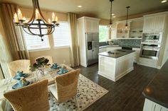 a kitchen and dining room with white cabinets, wood floors and chandelier hanging from the ceiling