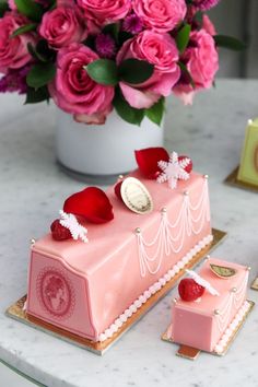 a pink cake sitting on top of a white table next to flowers and a vase filled with pink roses