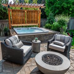 a hot tub sitting next to two chairs on top of a stone patio near a fire pit