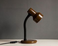 a brown desk lamp sitting on top of a white table next to a black cord