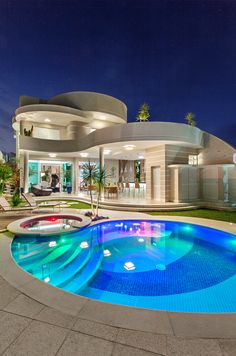 a house with a swimming pool in front of it at night, and an outdoor lounge area next to the pool