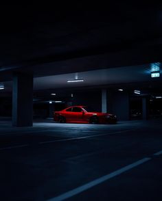 a red car parked in an empty parking garage at night with its lights turned on