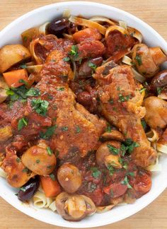 a white bowl filled with pasta and meat covered in marinara sauce on top of a wooden table