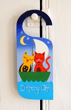 a door hanger with an image of two cats in a boat and the words drifting off on it