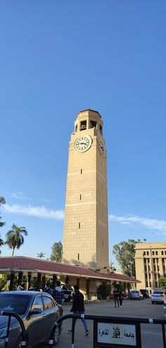 a tall clock tower sitting in the middle of a parking lot next to palm trees