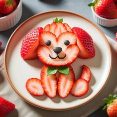 a plate with strawberries shaped like a dog on it's face and sitting in front of some strawberries