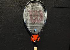 a tennis racket is hanging on the wall in front of a black background with red lettering