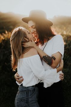 two women in white shirts and jeans hugging each other while the sun shines behind them